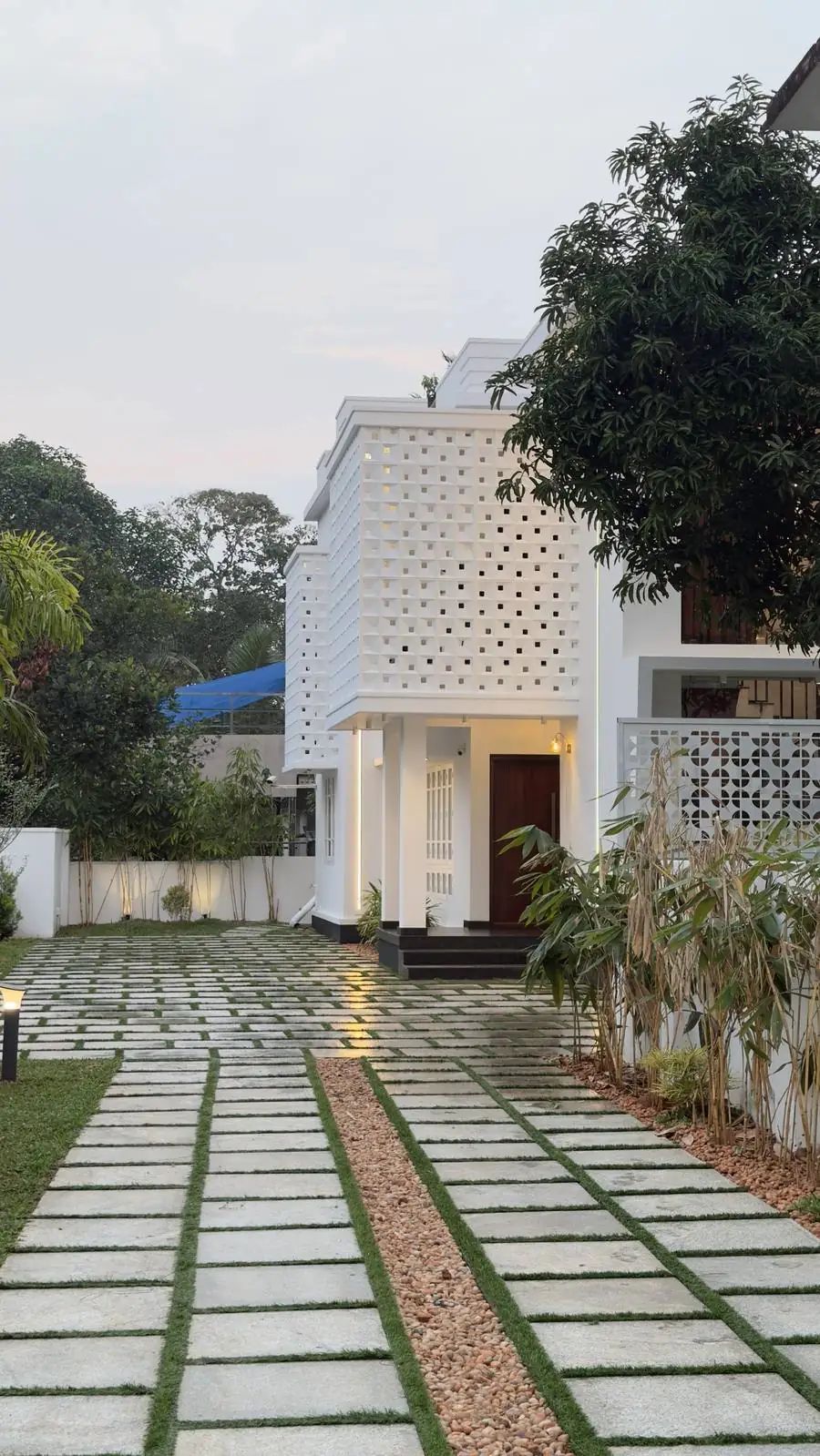 Granite slab driveway with grass joints leading to a white jali-facade house