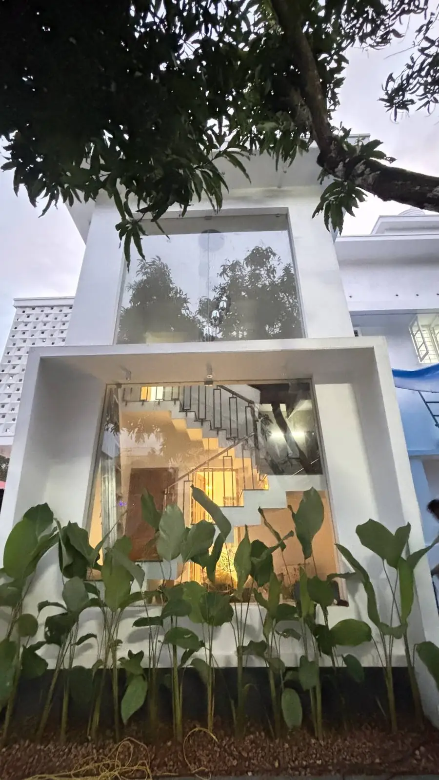 Double-height glass wall showing a lit staircase at dusk