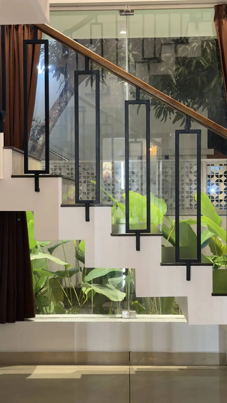 Staircase with black steel frame balusters and a timber rail over an indoor planter